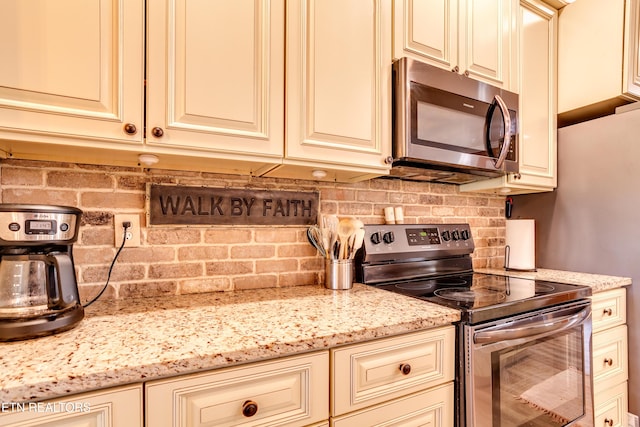 kitchen with cream cabinets, backsplash, light stone countertops, and stainless steel appliances