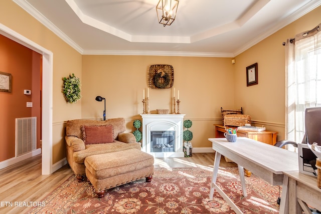 living area featuring a raised ceiling, wood finished floors, a glass covered fireplace, and visible vents