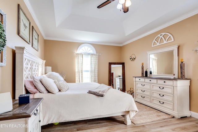 bedroom featuring a tray ceiling, light wood-type flooring, ceiling fan, and ornamental molding