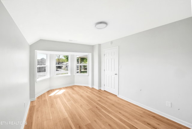 empty room with baseboards, vaulted ceiling, and light wood-style floors