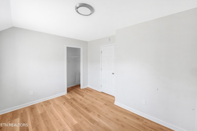unfurnished bedroom with a closet, light wood finished floors, baseboards, and vaulted ceiling