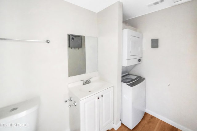 half bathroom featuring stacked washer and dryer, vanity, visible vents, toilet, and wood finished floors
