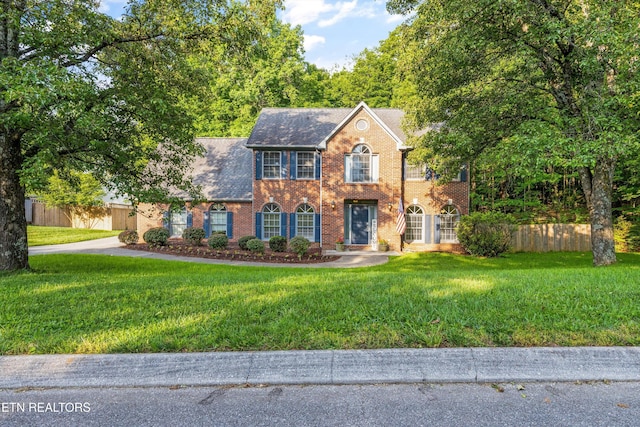 colonial house featuring fence, a front lawn, and brick siding