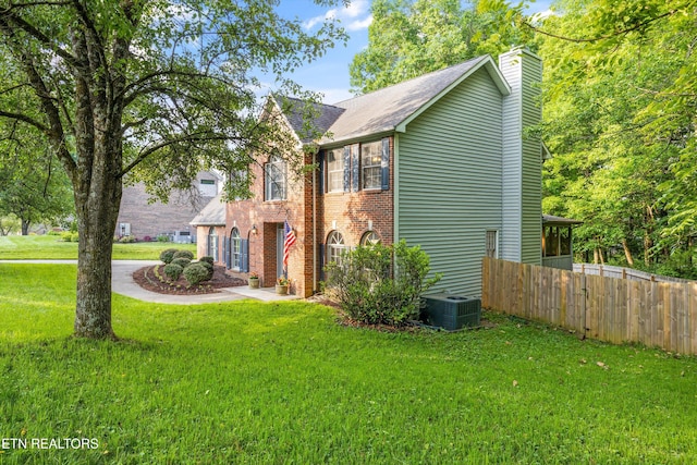 view of front of home with fence, brick siding, a front yard, central AC unit, and a chimney