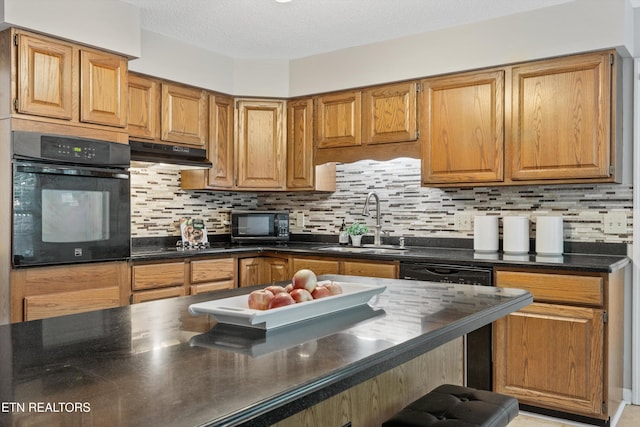 kitchen with dark countertops, under cabinet range hood, tasteful backsplash, a sink, and black appliances