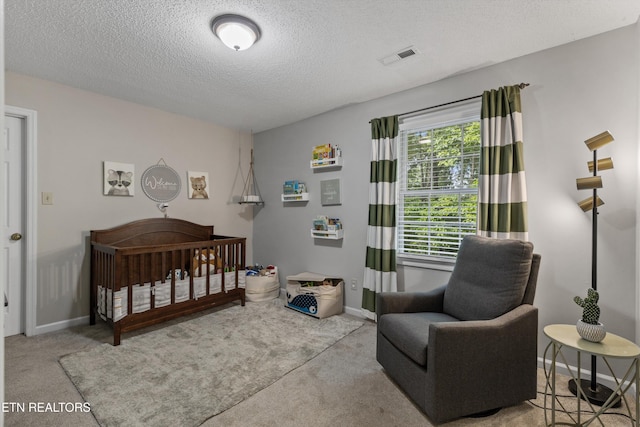 carpeted bedroom with visible vents, baseboards, a textured ceiling, and a crib