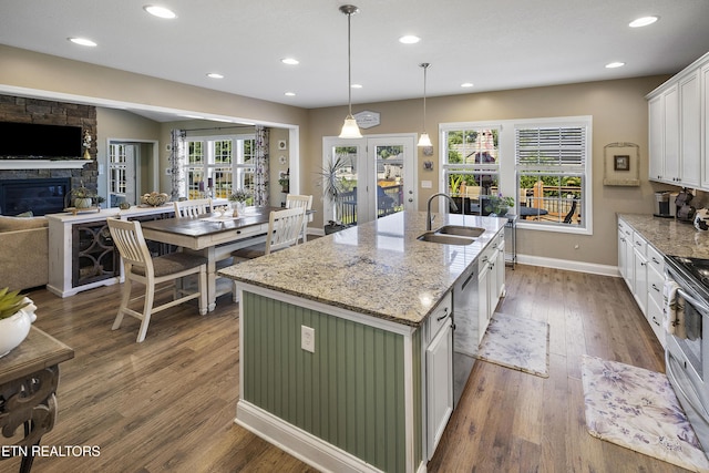 kitchen featuring white cabinets, a sink, dark wood-style flooring, a fireplace, and a center island with sink