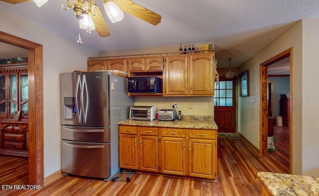 kitchen featuring stainless steel fridge with ice dispenser, black microwave, a textured ceiling, light wood-style floors, and brown cabinetry