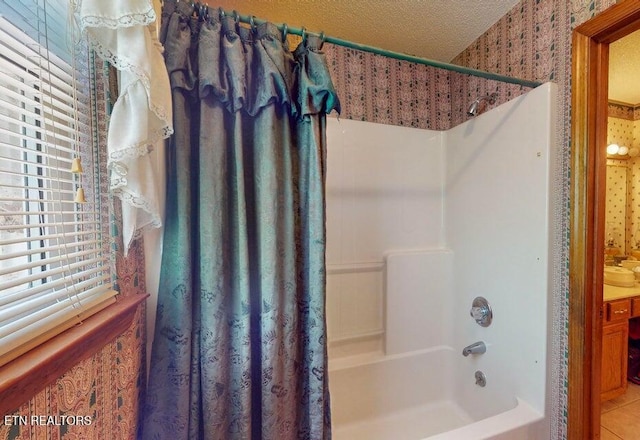 full bath featuring shower / bath combo, a textured ceiling, a sink, and wallpapered walls