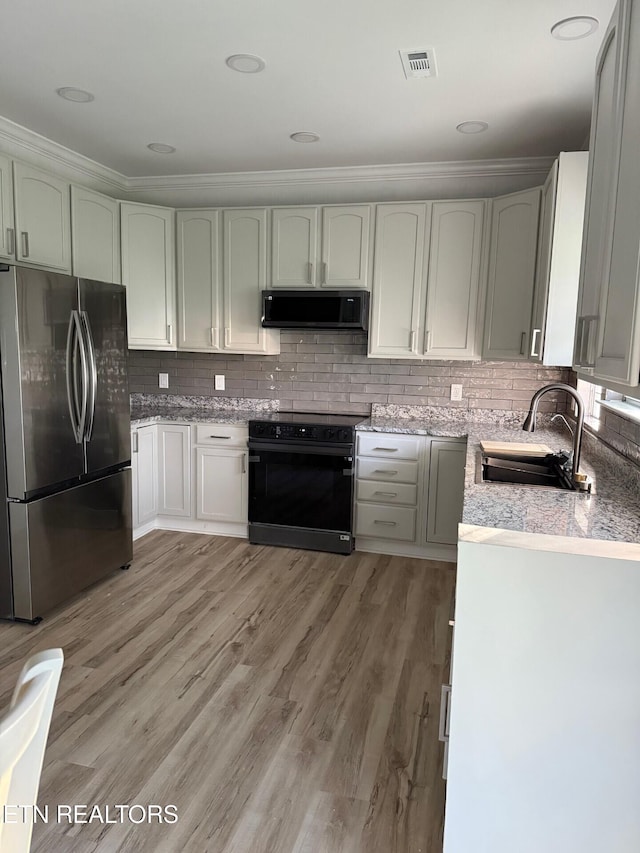 kitchen with black / electric stove, freestanding refrigerator, crown molding, visible vents, and a sink