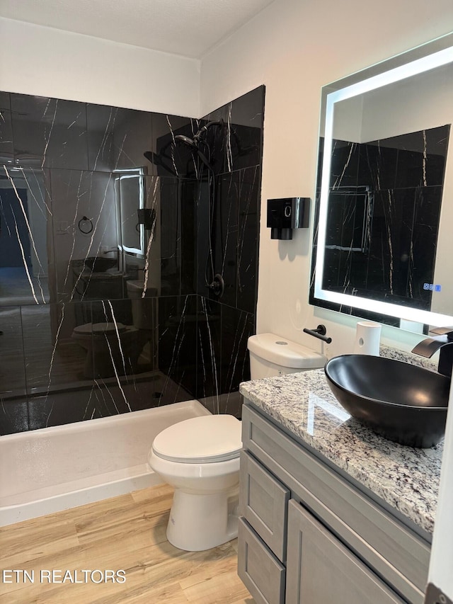 full bathroom with toilet, wood finished floors, a marble finish shower, and vanity