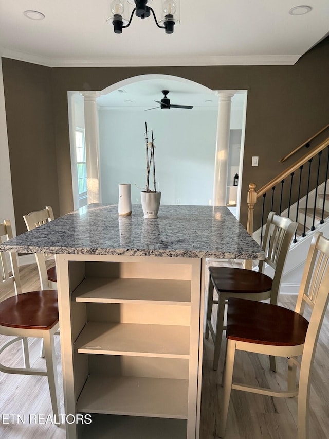 dining area with ceiling fan with notable chandelier, ornate columns, arched walkways, ornamental molding, and wood finished floors