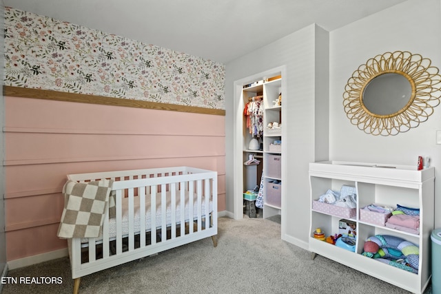 bedroom featuring carpet flooring, wainscoting, wallpapered walls, a walk in closet, and a nursery area