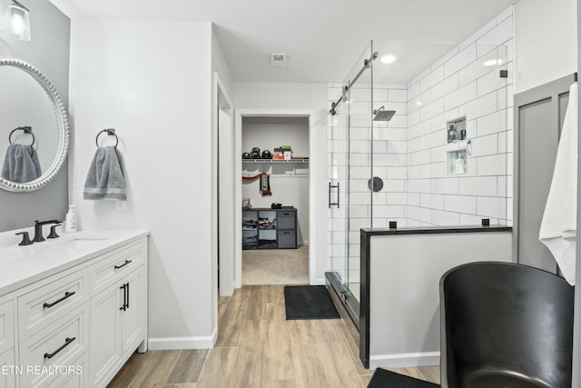 full bath with a spacious closet, a shower stall, vanity, and wood finished floors