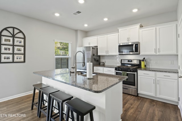 kitchen with tasteful backsplash, white cabinetry, a breakfast bar, appliances with stainless steel finishes, and a center island with sink