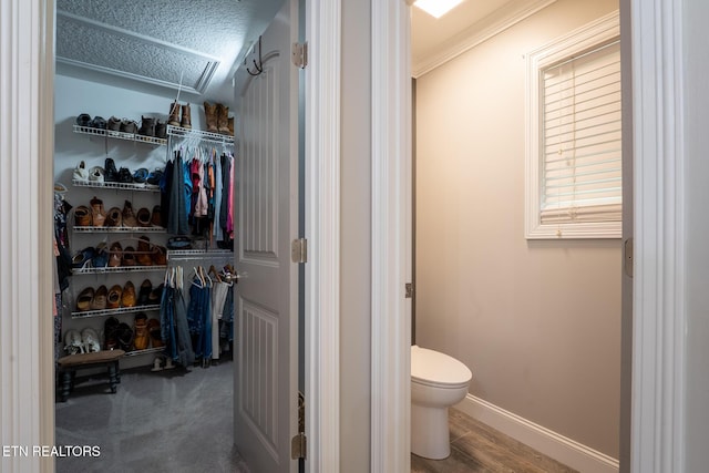 bathroom featuring toilet, baseboards, wood finished floors, crown molding, and a walk in closet