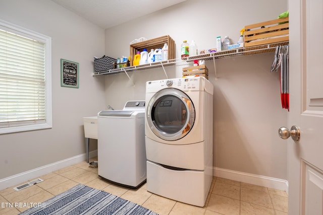 clothes washing area featuring light tile patterned flooring, laundry area, washing machine and dryer, baseboards, and visible vents