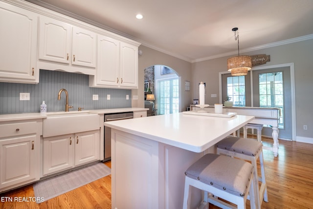 kitchen featuring stainless steel dishwasher, arched walkways, light wood-style floors, and a kitchen breakfast bar