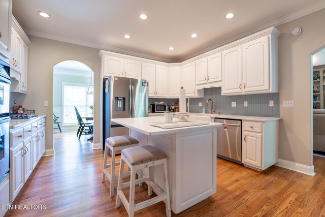 kitchen featuring arched walkways, white cabinetry, appliances with stainless steel finishes, and crown molding