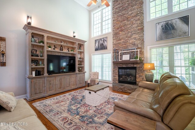 living room with ceiling fan, a stone fireplace, a towering ceiling, and plenty of natural light