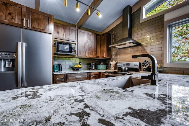 kitchen with light stone counters, stainless steel appliances, backsplash, vaulted ceiling, and wall chimney range hood