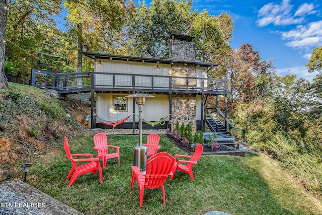 back of house featuring a lawn, stone siding, a deck, a fire pit, and stairs