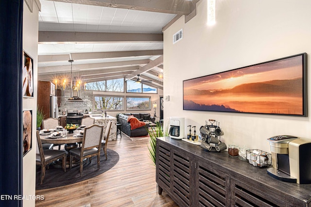 dining room featuring a ceiling fan, wood finished floors, visible vents, and vaulted ceiling with beams