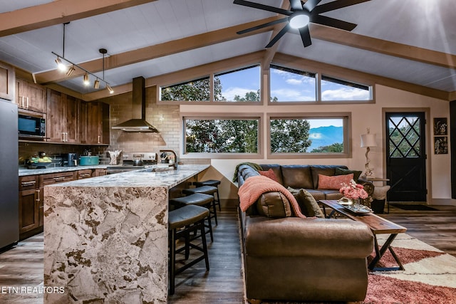 kitchen featuring light stone counters, wood finished floors, a breakfast bar area, stainless steel appliances, and wall chimney exhaust hood