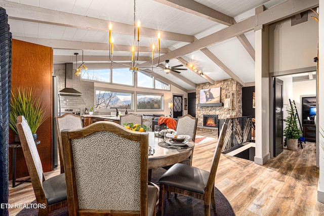 dining room featuring lofted ceiling with beams, a ceiling fan, wood finished floors, and a fireplace
