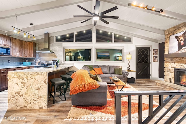 living room featuring a fireplace, light wood finished floors, a ceiling fan, and lofted ceiling with beams
