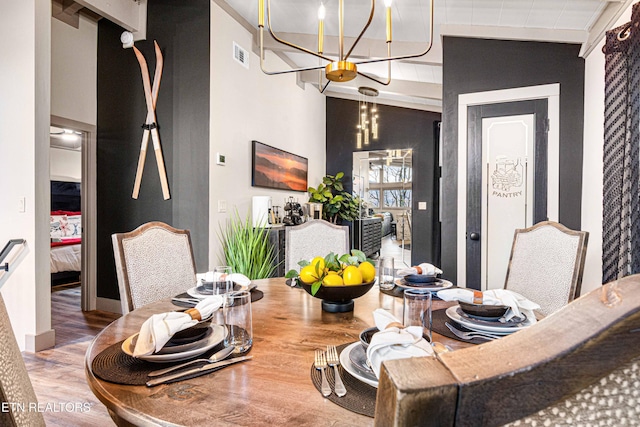 dining area featuring an accent wall, wood finished floors, baseboards, a notable chandelier, and visible vents