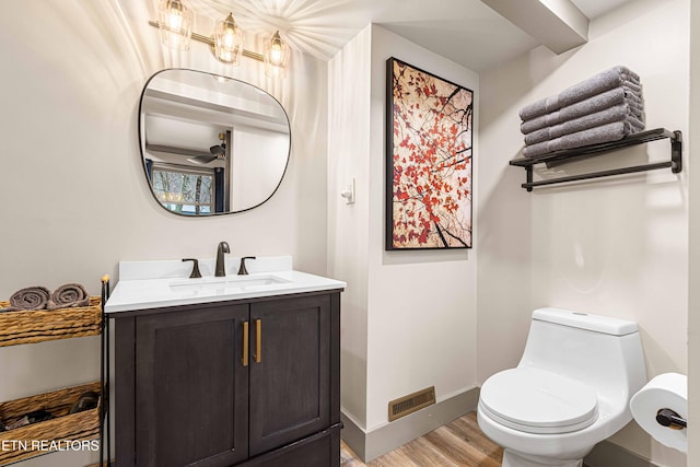 bathroom featuring toilet, baseboards, visible vents, wood finished floors, and vanity