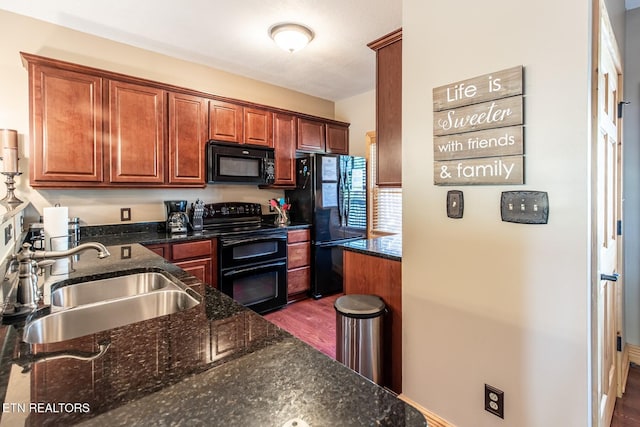 kitchen with a sink, dark wood finished floors, dark stone counters, and black appliances