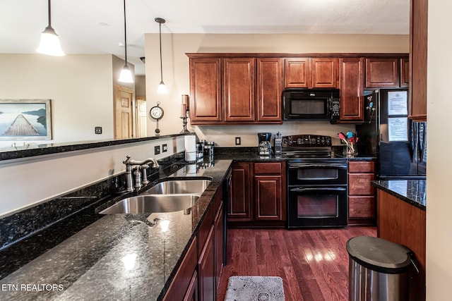 kitchen featuring hanging light fixtures, a sink, dark wood finished floors, dark stone counters, and black appliances