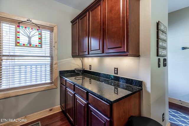 kitchen featuring baseboards, dark wood finished floors, and dark stone countertops