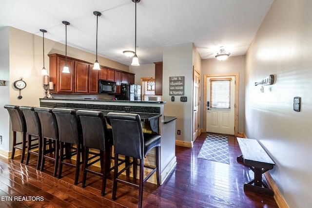 kitchen featuring a breakfast bar, black appliances, dark countertops, and dark wood-style floors