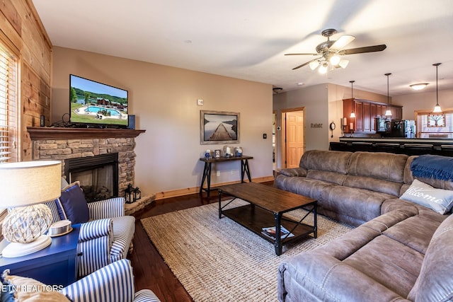 living area featuring a ceiling fan, baseboards, wood finished floors, and a fireplace