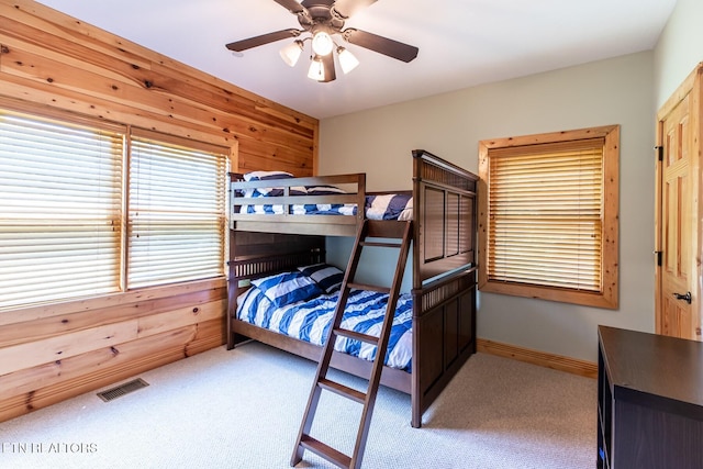 bedroom with wooden walls, carpet, a ceiling fan, and visible vents