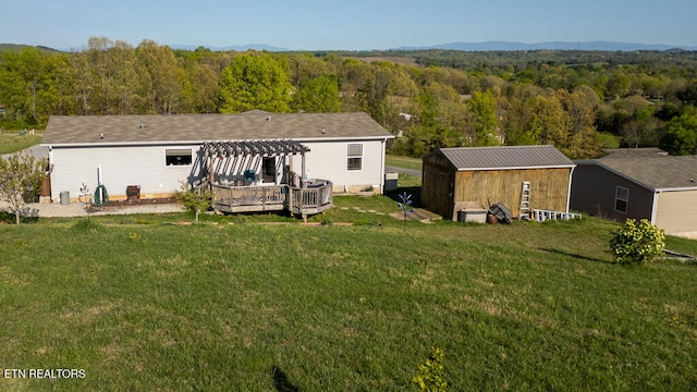 rear view of property with a deck, a pergola, a wooded view, a lawn, and an outbuilding