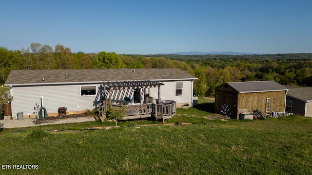 back of house with a view of trees, a pergola, a shed, an outbuilding, and a lawn