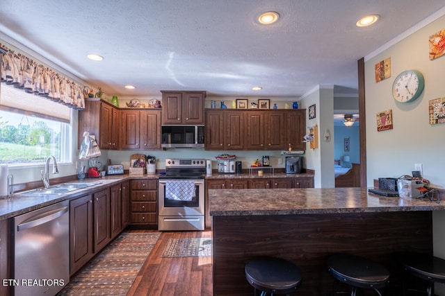 kitchen featuring a sink, appliances with stainless steel finishes, a kitchen breakfast bar, a peninsula, and dark wood finished floors