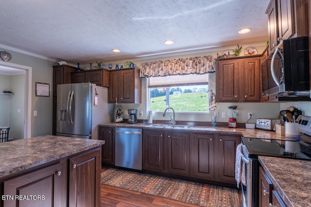 kitchen featuring appliances with stainless steel finishes, a sink, dark wood finished floors, and dark countertops