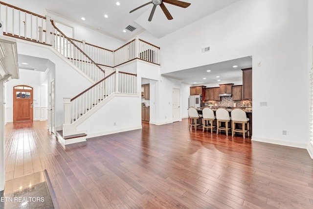 living room featuring dark wood-type flooring, a towering ceiling, visible vents, and a ceiling fan