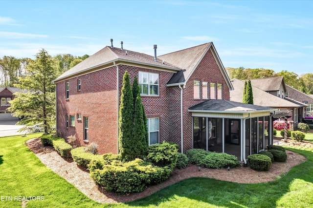 back of property with brick siding, a sunroom, and a lawn