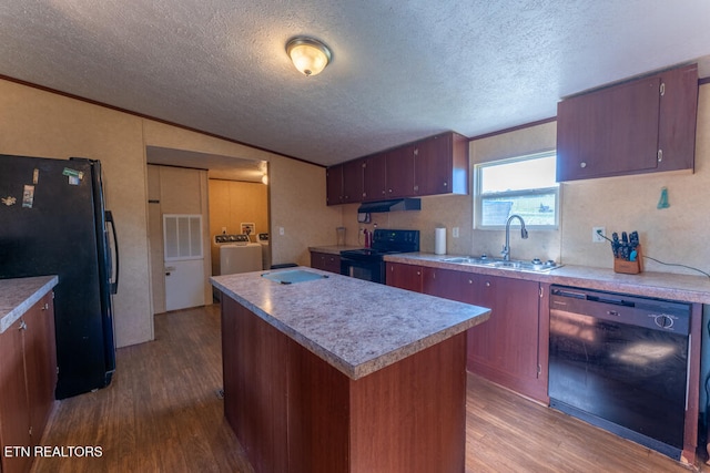 kitchen with a sink, under cabinet range hood, dark wood-style floors, black appliances, and washing machine and dryer