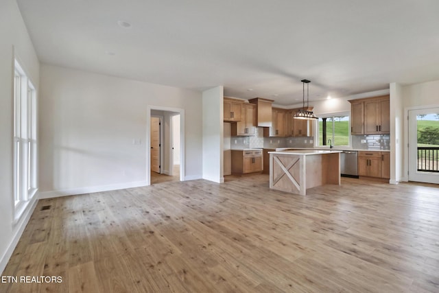 kitchen featuring stainless steel dishwasher, a kitchen island, light wood-type flooring, light countertops, and tasteful backsplash
