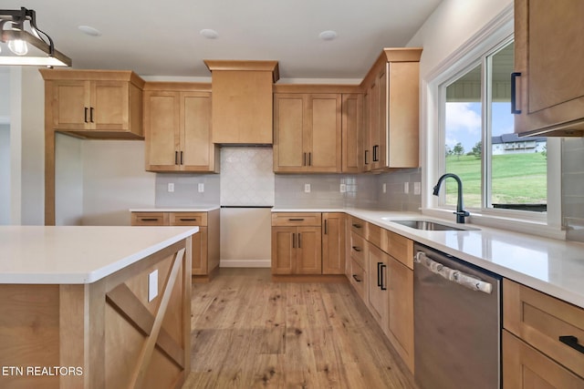 kitchen featuring decorative backsplash, dishwasher, a sink, light countertops, and light wood finished floors