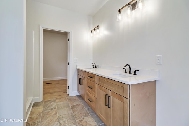 full bath featuring baseboards, a sink, stone finish floor, and double vanity