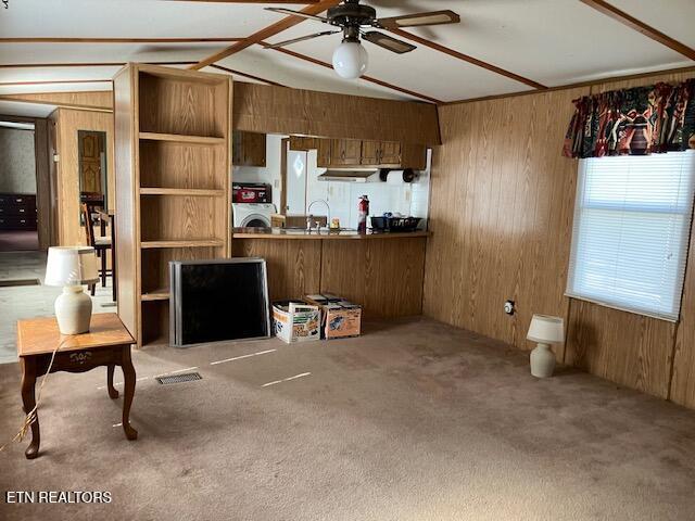 living room with ceiling fan, carpet, washer / clothes dryer, vaulted ceiling, and wood walls