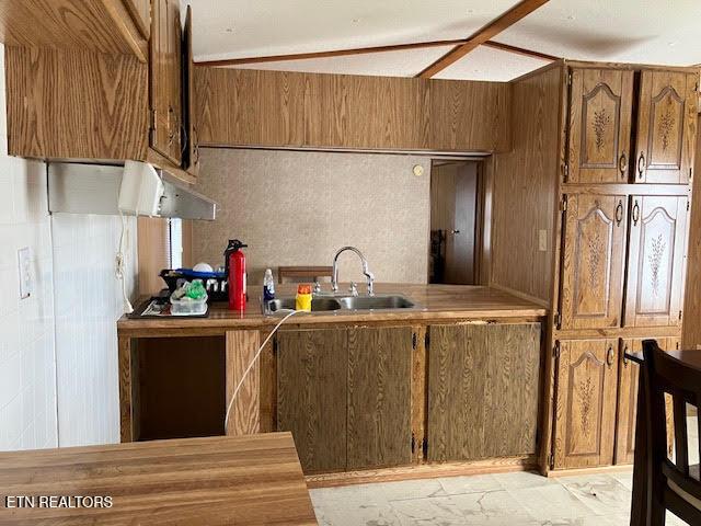 kitchen featuring a sink, light countertops, brown cabinetry, and wooden walls